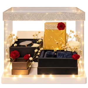 Clear acrylic display box with a crystal band and fairy lights, holding gift boxes, a gold box and red and white roses