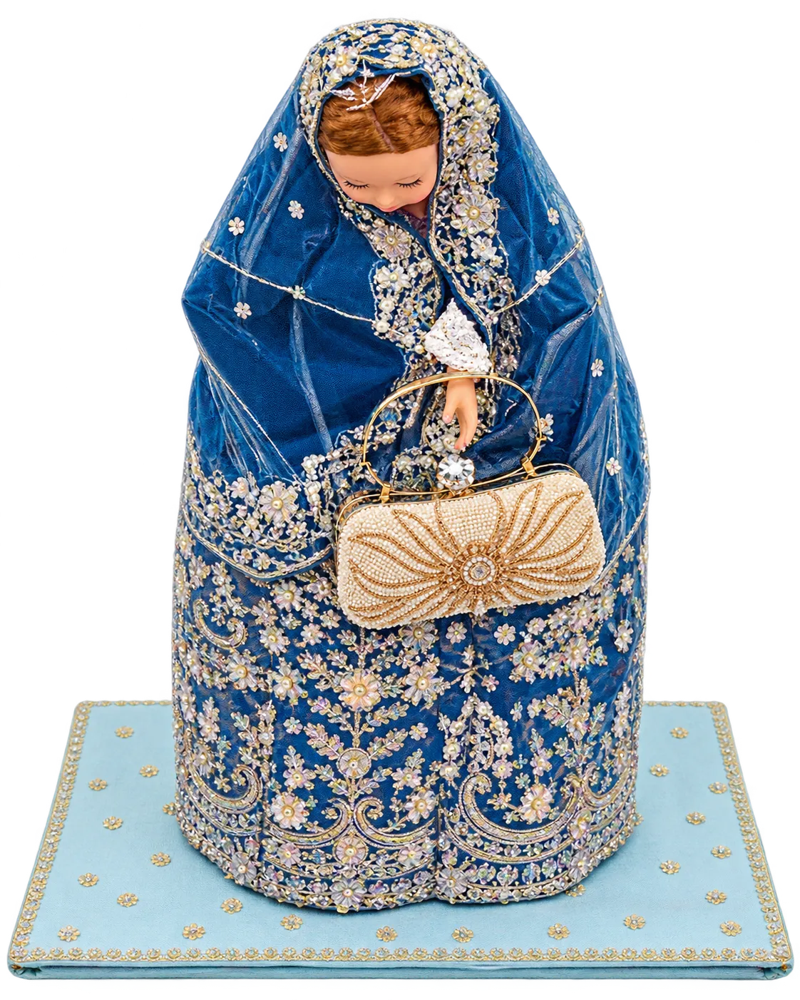 Embroidered blue outfit draped on a doll form holding a beaded clutch, on a light blue embroidered base