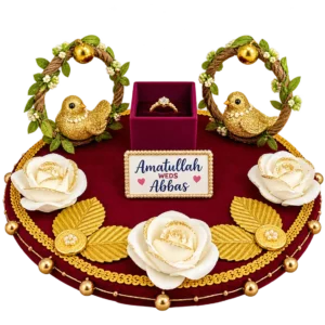 Round maroon velvet ring tray with two gold birds in rope wreaths, a ring box, white roses, gold leaves and a name plaque
